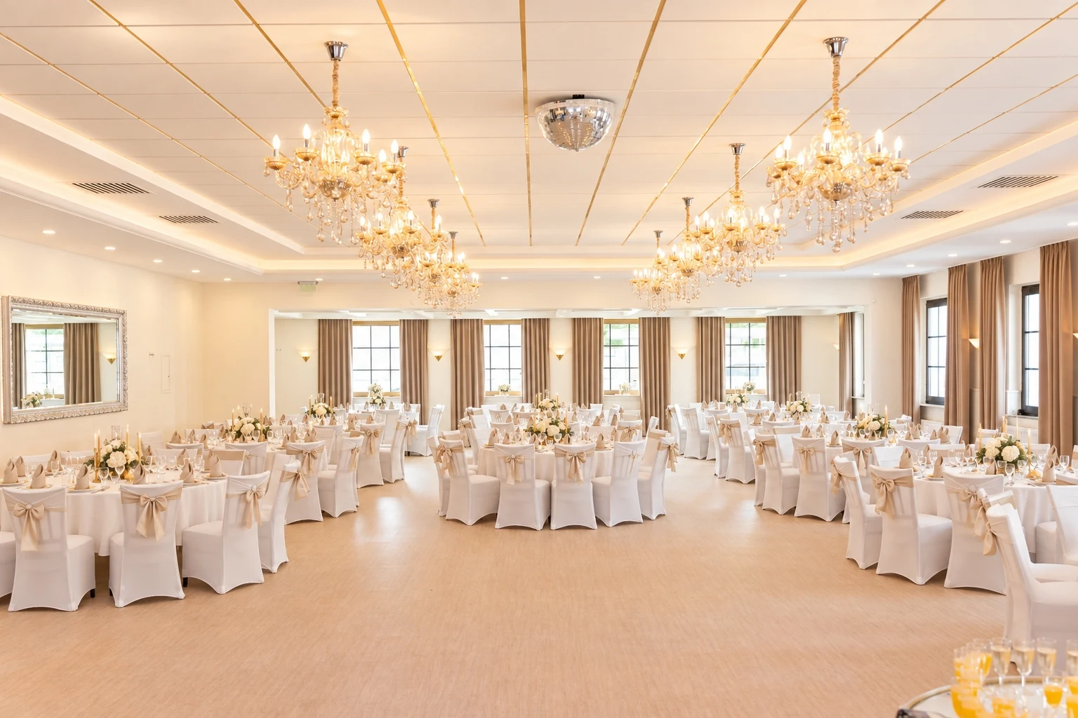 Festlich eingedeckter Saal mit runden Tischen, cremefarbenen Stuhlhussen und Kristallkronleuchtern in der Eventlocation Classic